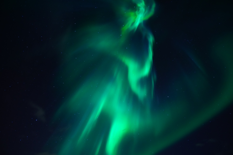 Aurora borealis curtains over a snow-covered cabin on a clear night near Levi during a northern lights holiday in Finnish Lapland